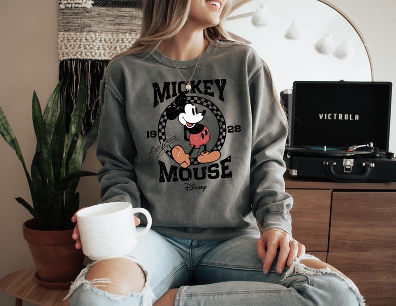 a woman in a mickey mouse sweatshirt holding a coffee mug