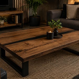 May include: A rectangular coffee table featuring a natural wood grain surface with a dark, central resin inlay. The table is supported by two sturdy, black metal U-shaped legs. A black candle and a small green plant sit on the wooden surface.