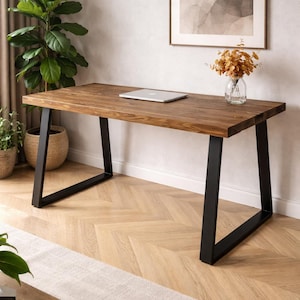 May include: A wooden desk with a rectangular top and black metal legs. A laptop sits on the desk. The desk is in a room with a plant, a framed picture, and a vase of dried flowers. The room has a light-colored rug and hardwood floors.