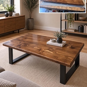 May include: A rectangular coffee table with a dark brown stained wood top featuring visible wood grain and knots, supported by two black metal U-shaped legs. A small book titled The Kinfolk Home and a small dark vase sit on the table surface.