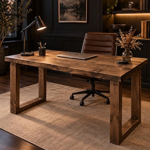 Op de afbeelding: Een rechthoekig houten bureau met een donkerbruine gebeitste afwerking en dikke, U-vormige poten. Het bureaublad bevat een zilveren laptop, een zwarte bureaulamp, een cilindrische pennenhouder met schrijfgerei en een glazen vaas met droogbloemen.