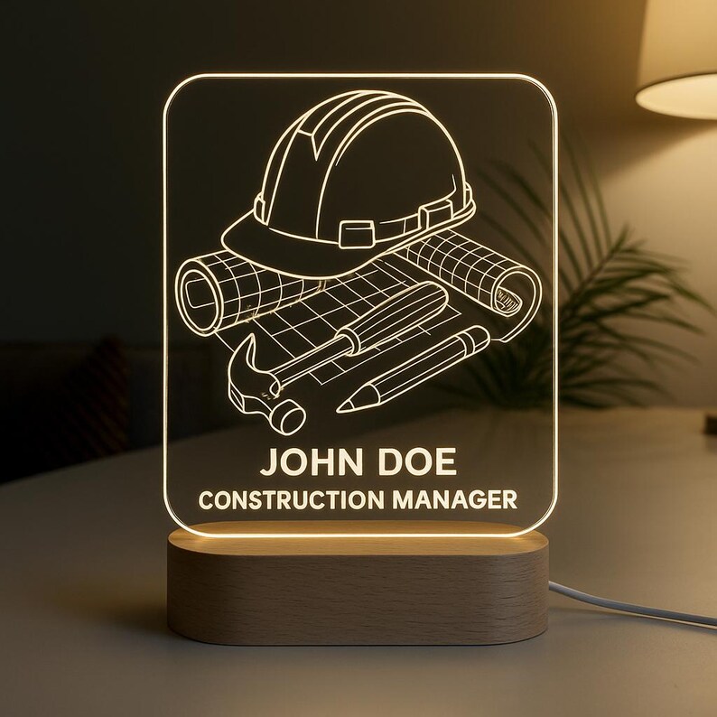 Peut inclure: Lampe de chevet personnalis&eacute;e sur le th&egrave;me de la construction. Elle pr&eacute;sente un casque de chantier, des plans et des outils, avec le nom "JOHN DOE" et le titre "CONSTRUCTION MANAGER". La lampe est pos&eacute;e sur un socle en bois.