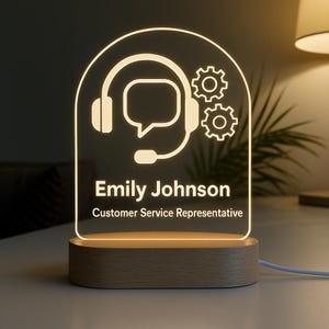 Peut inclure: Lampe de bureau personnalis&eacute;e avec une base en bois et un panneau en acrylique transparent. Le panneau pr&eacute;sente un graphisme blanc d'un casque, d'une bulle de dialogue et d'engrenages, avec le nom "Emily Johnson" et le titre "Customer Service Representative".