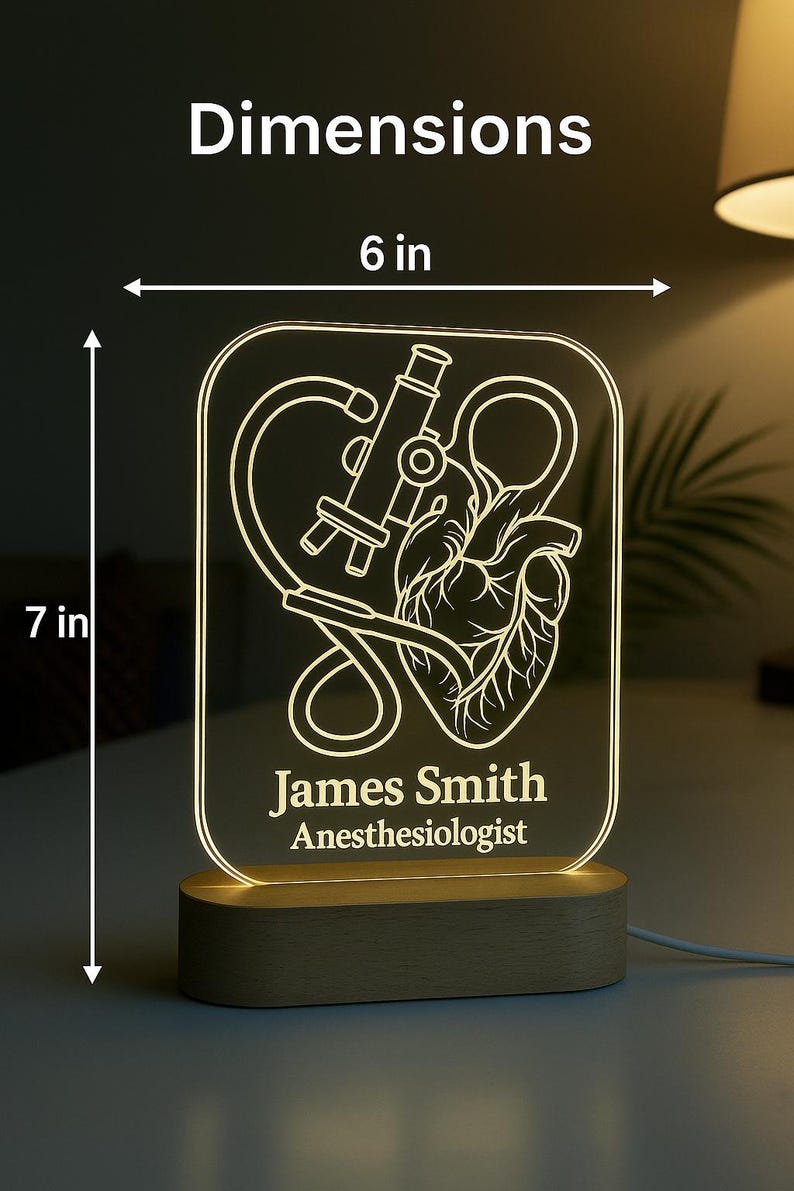 Peut inclure: Lampe LED rectangulaire avec une base en bois, pr&eacute;sentant un design m&eacute;dical. Le panneau lumineux affiche un microscope, un c&oelig;ur et le nom "James Smith, Anesth&eacute;siste". La lampe mesure 15 cm de large et 18 cm de haut.