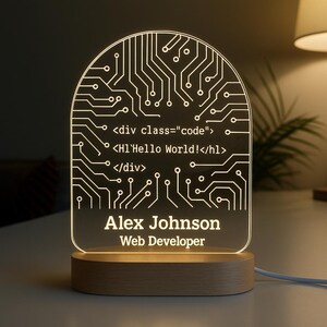 May include: A personalized LED desk lamp with a circuit board design. The lamp features the text "Alex Johnson, Web Developer" and code snippets. The lamp sits on a wooden base and emits a warm glow, perfect for a desk or nightstand.