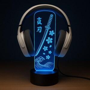 May include: A blue LED lamp with a katana sword design, cherry blossoms, and Japanese text. The lamp is paired with silver and black headphones. The lamp sits on a black base, creating a unique decorative piece.