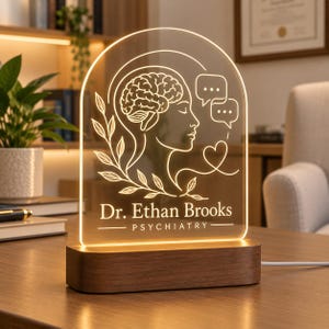 May include: An arched acrylic light sign with a wooden base featuring an engraved profile of a human head with a brain, speech bubbles, a heart, and a leafy branch. The text reads Dr. Ethan Brooks PSYCHIATRY in a clean, sans-serif font.
