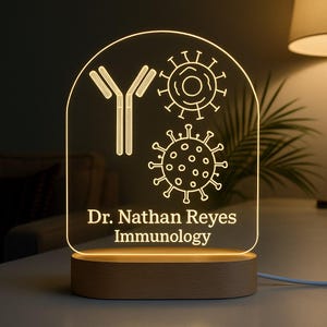 Puede incluir: Lámpara de escritorio acrílica iluminada y personalizada con base de madera. Muestra un anticuerpo en forma de Y, ilustraciones de virus y el texto "Dr. Nathan Reyes Immunology" en blanco. La lámpara emite una luz cálida.