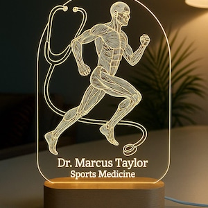 Puede incluir: Lámpara LED brillante con una figura corriendo con detalles musculares y un diseño de estetoscopio. La lámpara incluye el texto "Dr. Marcus Taylor Sports Medicine" sobre una base de madera.