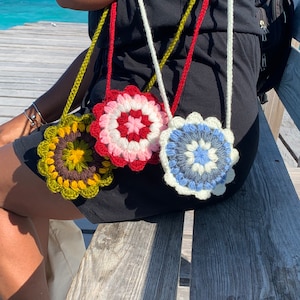 May include: Three crocheted flower-shaped purses with different colored patterns. The purses are attached to white, red, and green cords.