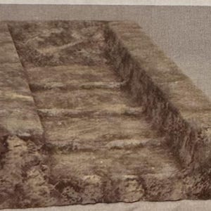 May include: A rectangular stone trough with a rough, textured surface. The trough has a channel running down the center, with steps carved into the sides.