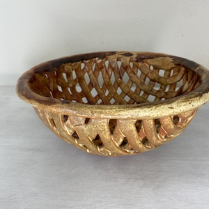 May include: A brown and tan ceramic bowl with a woven design. The bowl is handmade and has a rustic look.