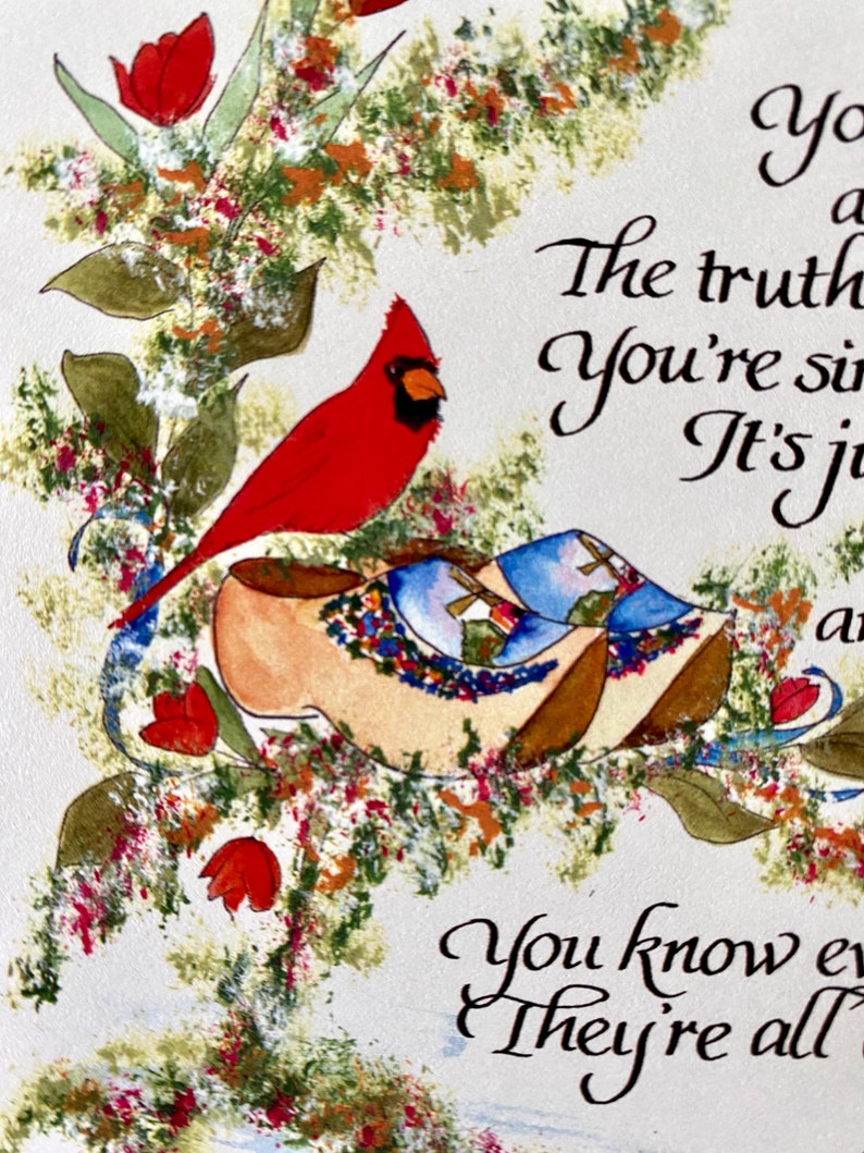May include: A red cardinal bird perched on top of two wooden clogs with floral designs. The background is a white surface with a handwritten message that reads "You know every one of them is a part of you. The truth is you're simply a part of them. It's just a matter of time. You know every one of them is a part of you. They're all a part of you."
