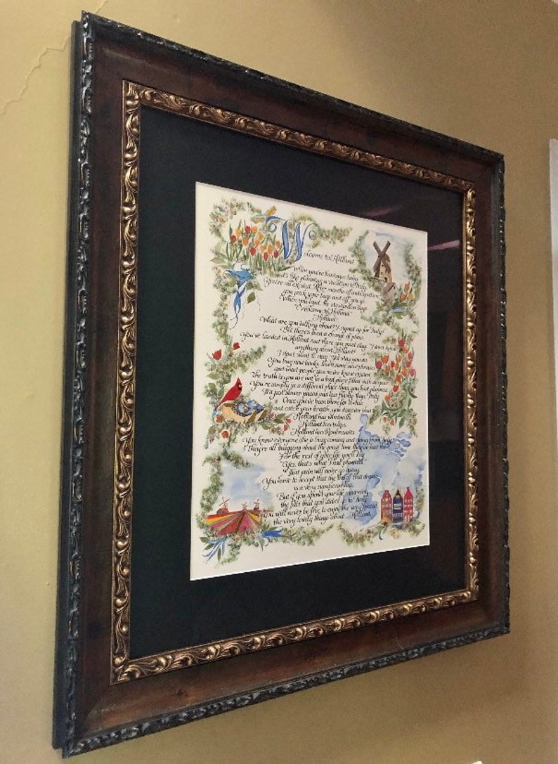 May include: A framed calligraphic artwork with a black mat and a brown wood frame. The artwork features a handwritten poem with illustrations of birds, flowers, and a windmill. The poem begins with the words "Welcome to the Wildwood".