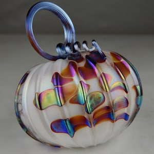 May include: A white glass pumpkin with iridescent, multi-colored swirls and a blue glass stem.