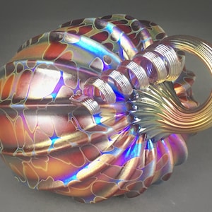 May include: A glass pumpkin with a swirling iridescent finish in shades of brown, gold, blue, and purple. The pumpkin has a textured surface and a twisted stem.