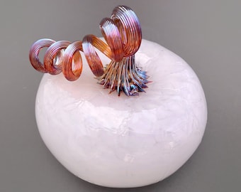 May include: A white glass pumpkin with a swirling, iridescent copper stem. The pumpkin has a textured surface.