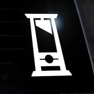 May include: White vinyl sticker of a guillotine on a black car window. The sticker is from Seward Street Studios.