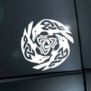 May include: A white vinyl decal of a Celtic knot design featuring three stylized birds in a circle. The decal is applied to the back window of a black car.