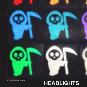 May include: Nine glow-in-the-dark Grim Reaper stickers in various colors, including red, orange, yellow, blue, purple, green, and white. The stickers are on a black background and feature the Grim Reaper holding a scythe. The text "HEADLIGHTS" is at the bottom of the image.