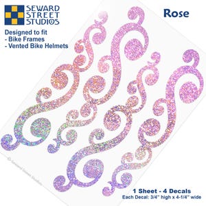 May include: A sheet of four pink glittery swirl decals labeled Rose. The text reads Seward Street Studios, Designed to fit Bike Frames and Vented Bike Helmets. Each decal measures 3/4 inches high by 4-1/4 inches wide on the sheet.