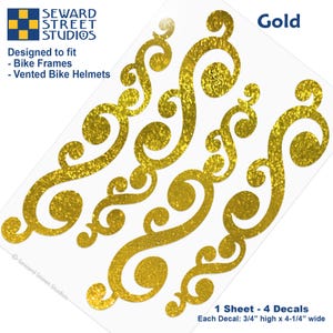 May include: A sheet of four gold glitter decals with swirling scroll patterns. The text reads Seward Street Studios, Designed to fit Bike Frames and Vented Bike Helmets, Gold, and 1 Sheet - 4 Decals, Each Decal: 3/4" high x 4-1/4" wide.