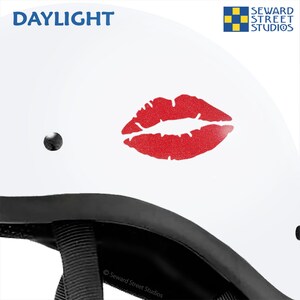 May include: White motorcycle helmet with a red glitter lips decal. The helmet has a black strap and the text "DAYLIGHT" and "Seward Street Studios" are visible.