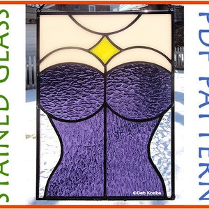 Puede incluir: Un diseño de vitral que presenta un corsé morado con un diamante amarillo en el centro. El diseño está enmarcado en negro y se coloca sobre un fondo nevado.