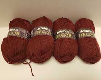 May include: Four skeins of Patons Decor yarn in a deep burgundy color. Each skein has a label with the brand name and the words "Decor" in gold lettering.
