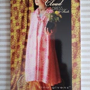 May include: A product advertisement features a young person wearing a pink floral dress with matching pants. The dress has a ruffled neckline and a flowing silhouette. The text "Cloud Dress & Pants" is visible, along with the brand name "tina givens". The background includes patterned curtains.