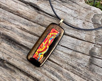 May include: A rectangular glass pendant with a black frame and a red, yellow, and blue pattern inside. The pendant is hanging from a black cord.