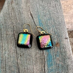 May include: A pair of iridescent glass square earrings with gold hooks. The glass is a mix of pink, blue, green, and yellow.