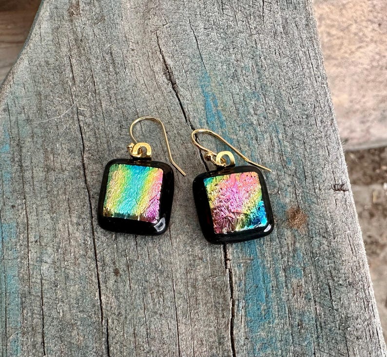May include: A pair of iridescent glass square earrings with gold hooks. The glass is a mix of pink, blue, green, and yellow.