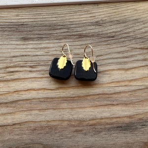 May include: A pair of black square earrings with gold accents. The earrings have a simple, geometric design.