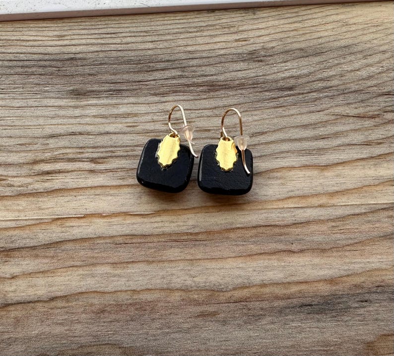 May include: A pair of black square earrings with gold accents. The earrings have a simple, geometric design.