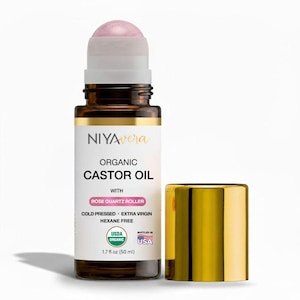 May include: A brown glass bottle of organic castor oil with a rose quartz roller and a gold cap. The label reads "NIYAvera ORGANIC CASTOR OIL" and "1.7 fl oz (50 ml)". The product is cold pressed, extra virgin, and hexane free.