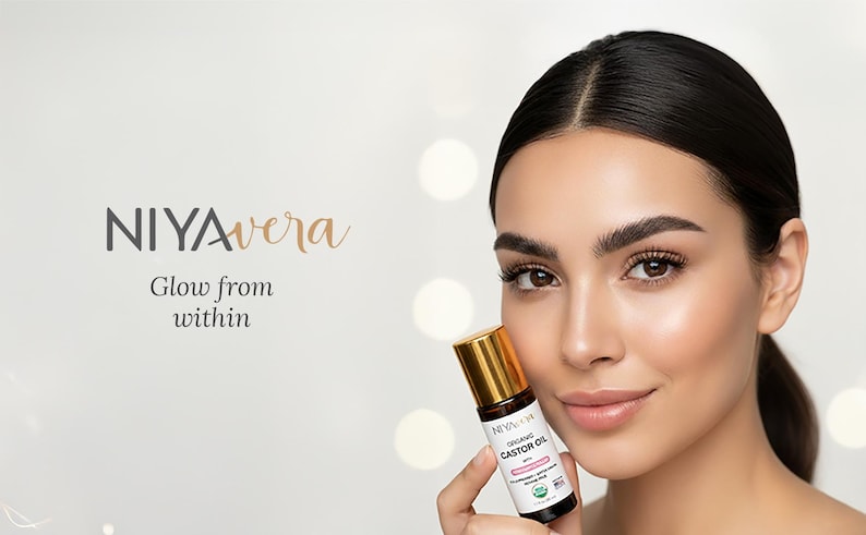 Puede incluir: Una mujer sostiene un peque&ntilde;o frasco de aceite de ricino org&aacute;nico con tapa dorada. El frasco lleva la etiqueta "NIYAvera" y "Glow from within". El fondo es blanco suave y borroso con luces bokeh.