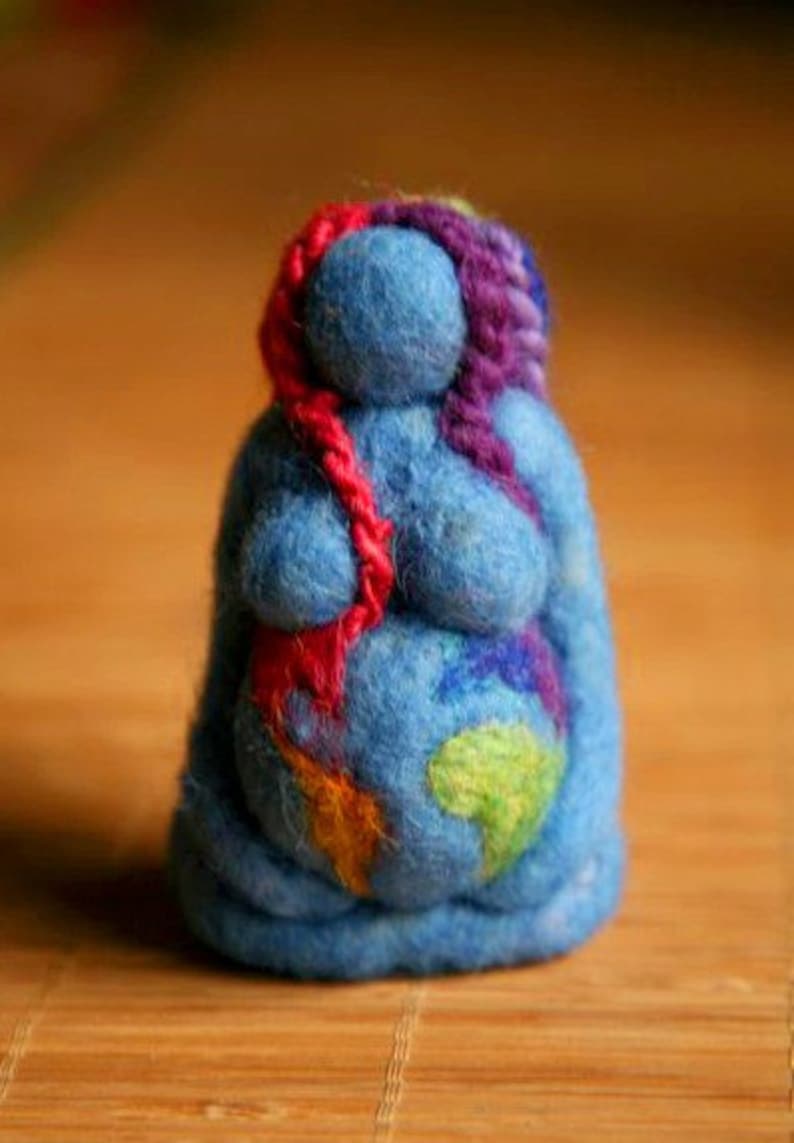 May include: A blue felt doll with a colorful design on its belly. The doll has a red, purple, and pink yarn hair.