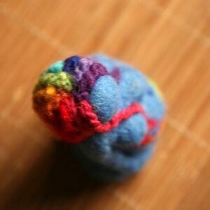 May include: A small, blue, felt ball with a colorful, rainbow-colored yarn wrapped around it.