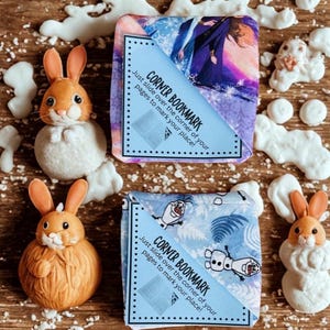 Puede incluir: Dos marcap&aacute;ginas de esquina con texto, "CORNER BOOKMARK, Just slide over the corner of your pages to mark your place!" y dos figuras de conejito. Un marcap&aacute;ginas tiene un dise&ntilde;o morado y azul, el otro tiene un dise&ntilde;o azul y blanco.