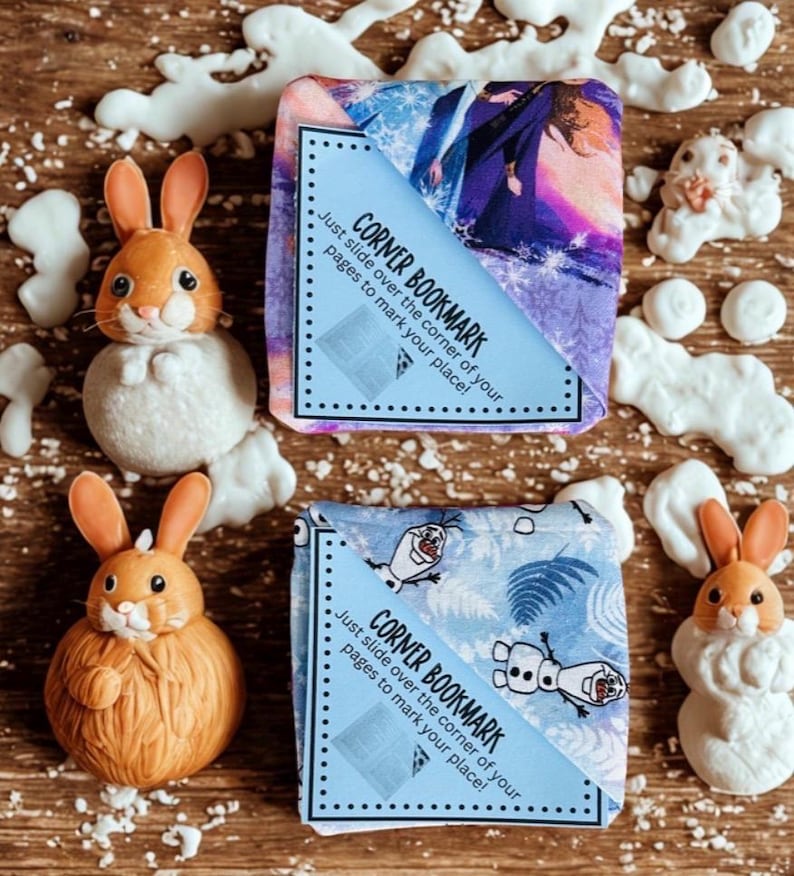 Puede incluir: Dos marcap&aacute;ginas de esquina con texto, "CORNER BOOKMARK, Just slide over the corner of your pages to mark your place!" y dos figuras de conejito. Un marcap&aacute;ginas tiene un dise&ntilde;o morado y azul, el otro tiene un dise&ntilde;o azul y blanco.