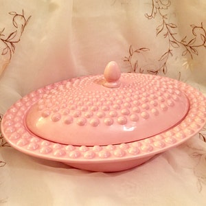 May include: A pink ceramic serving dish with a lid. The dish and lid are covered in small raised dots.