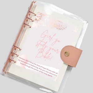 May include: A clear plastic binder with a pink and gold design. The binder has a quote that says "Girl, go study your Bible!" and a Bible verse from Romans 15:13.