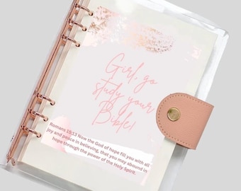 May include: A clear plastic binder with a pink and gold design. The binder has a quote that says "Girl, go study your Bible!" and a Bible verse from Romans 15:13.