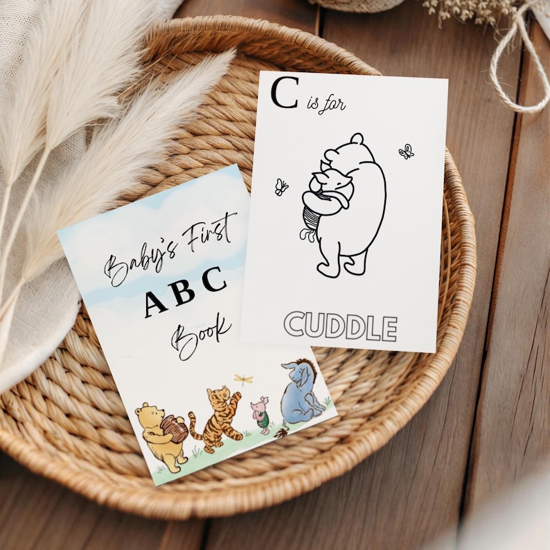 May include: Two children's books in a woven basket. One book is titled "Baby's First ABC Book" with illustrations of Winnie the Pooh characters. The other card says "C is for Cuddle" with a Winnie the Pooh illustration.