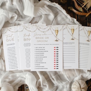 May include: A set of white bridal shower game cards with gold detailing and champagne glass illustrations. The cards feature games such as "Find the Guest", "Bride Bingo", and "Guess Who: Bride or Groom?" The cards are displayed on a white fabric background.