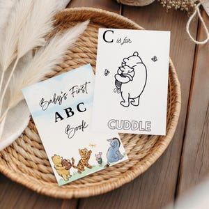 May include: A children's ABC book and flashcards featuring Winnie the Pooh characters. The ABC book reads "Baby's First ABC Book". The flashcard shows Winnie the Pooh hugging Piglet with the word "CUDDLE" below.