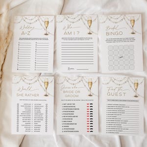 May include: Six bridal shower game cards with champagne glasses and pearl decorations. The cards include games such as "Wedding A-Z", "Who Am I?", and "Bridal Bingo". The design uses a white and gold colour scheme.