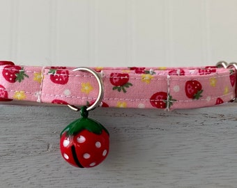 Pode incluir: Coleira de gato rosa com estampa de morango e um pequeno sino em forma de morango.