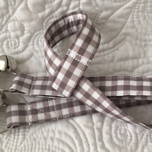 May include: A grey and white gingham ribbon with four silver bells attached. The ribbon is folded in half and the bells are hanging from the loop.